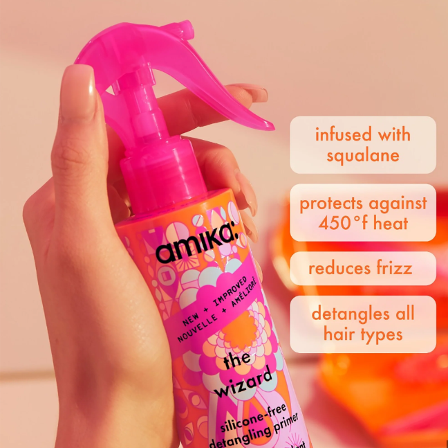 Hand holding a pink spray bottle labeled 'amika' with product features displayed.