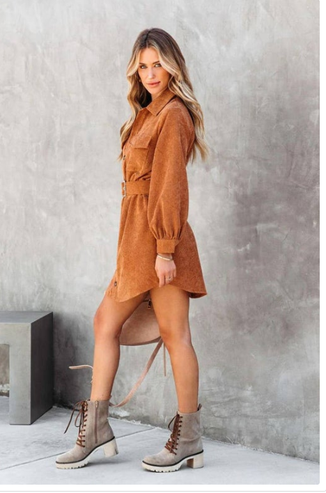 Woman wearing a brown dress and gray boots against a gray wall.