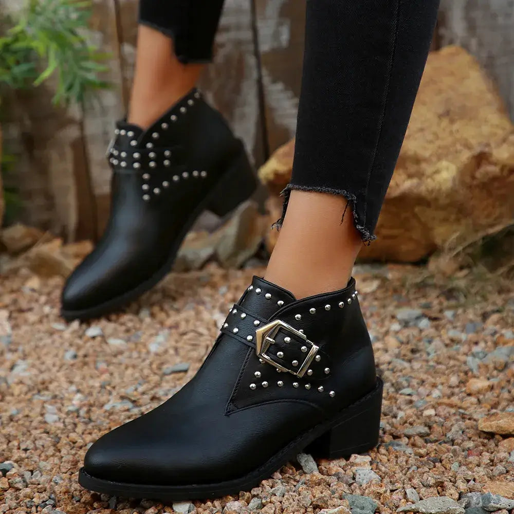 Black studded ankle boots worn outdoors on a rocky surface