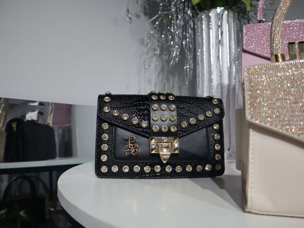 Black studded handbag on a white surface with a blurred background