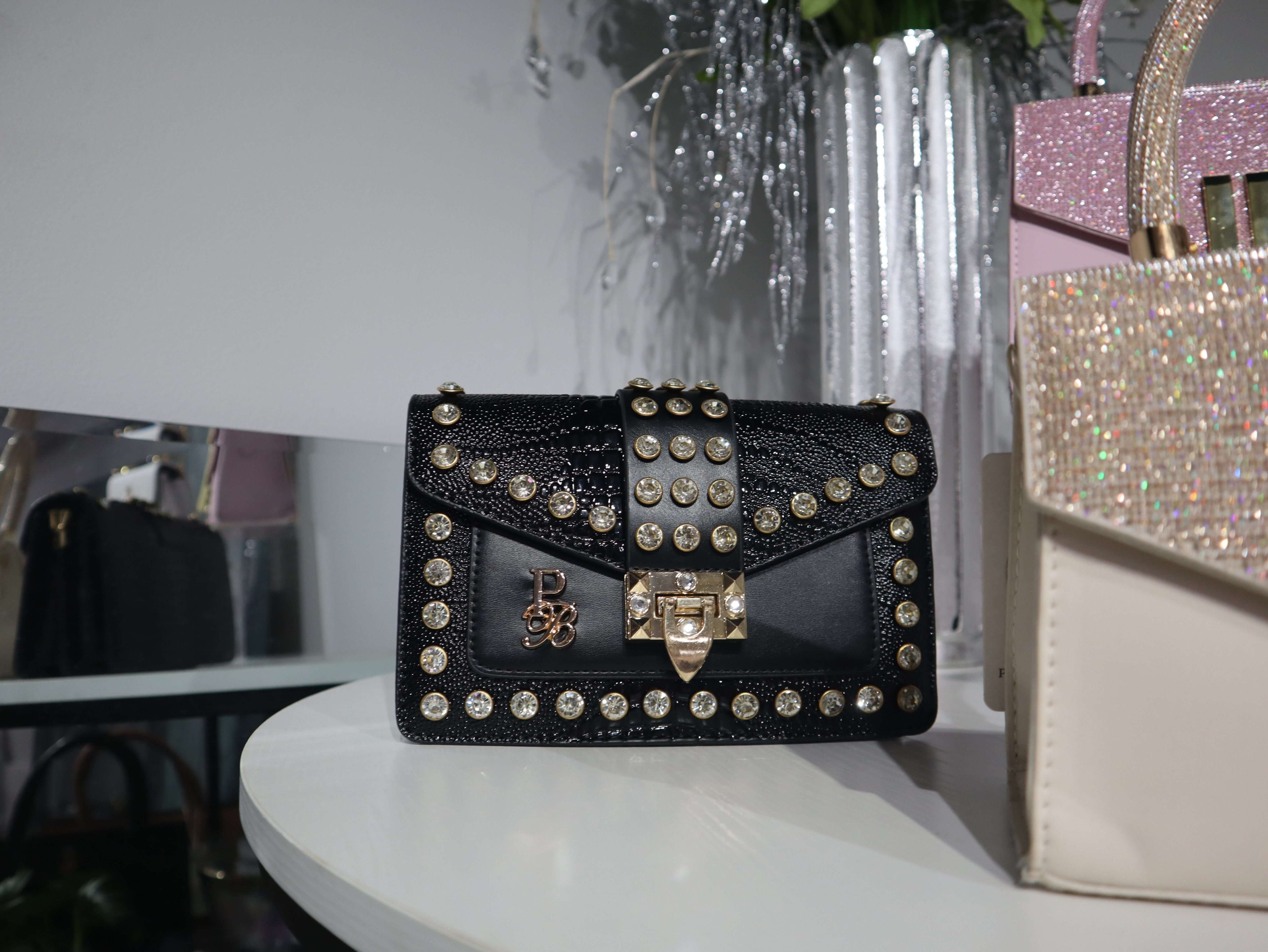 Black studded handbag on a white surface with a blurred background