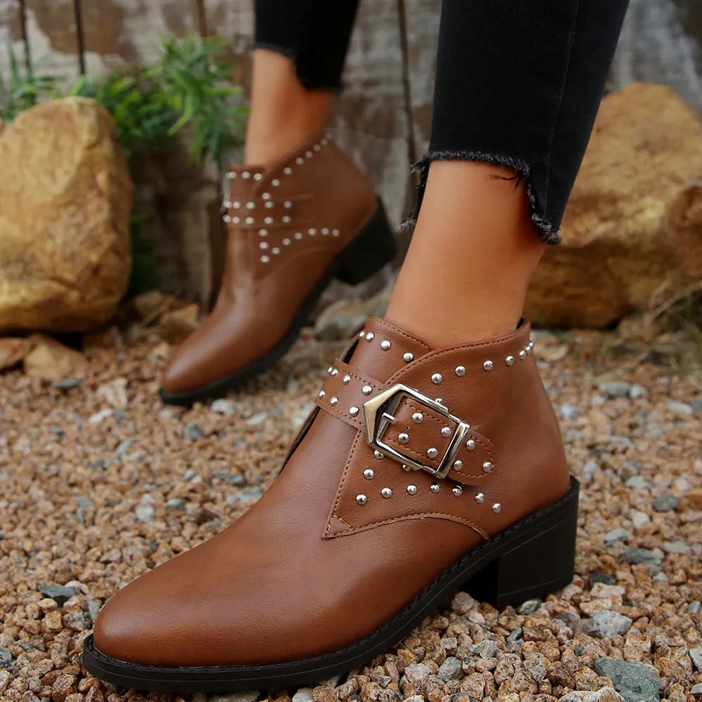 Brown studded ankle boots worn outdoors on a rocky ground.