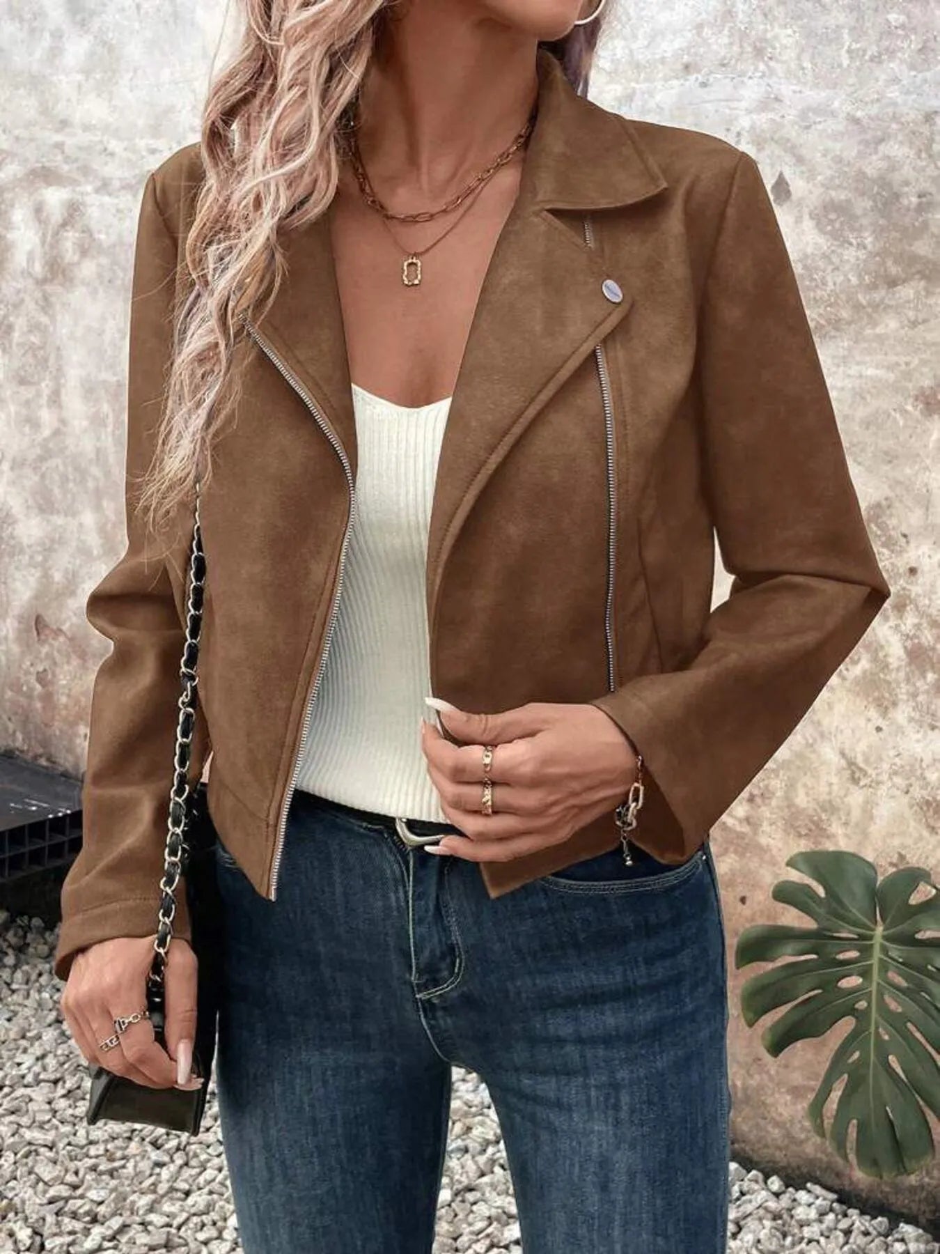 Person wearing a brown suede jacket over a white top and blue jeans, standing against a neutral background.