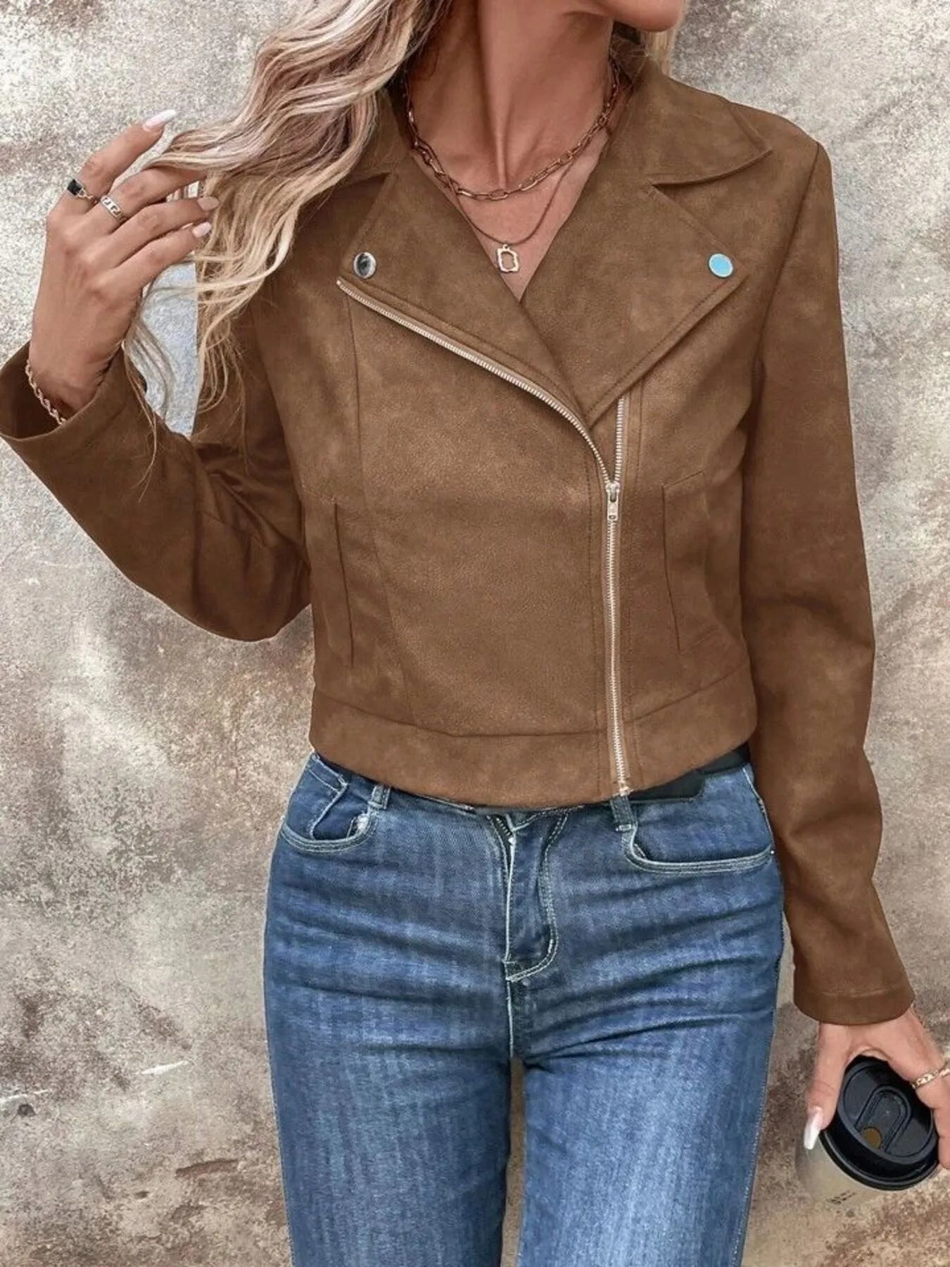 Person wearing a brown suede jacket and blue jeans against a neutral background