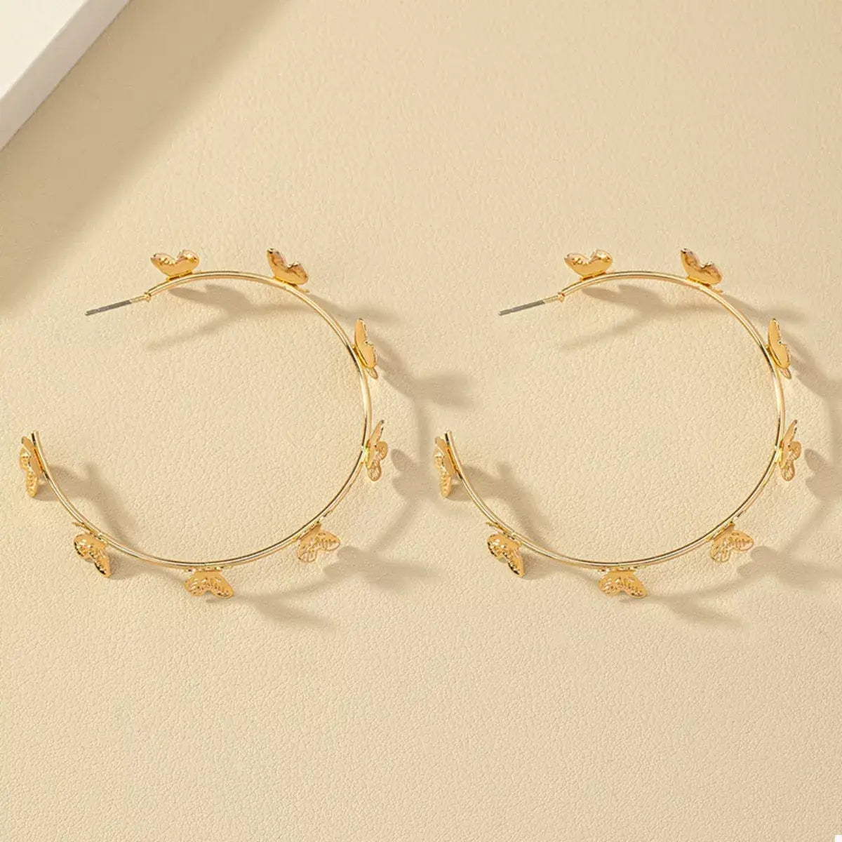 Gold hoop earrings with floral designs on a beige background