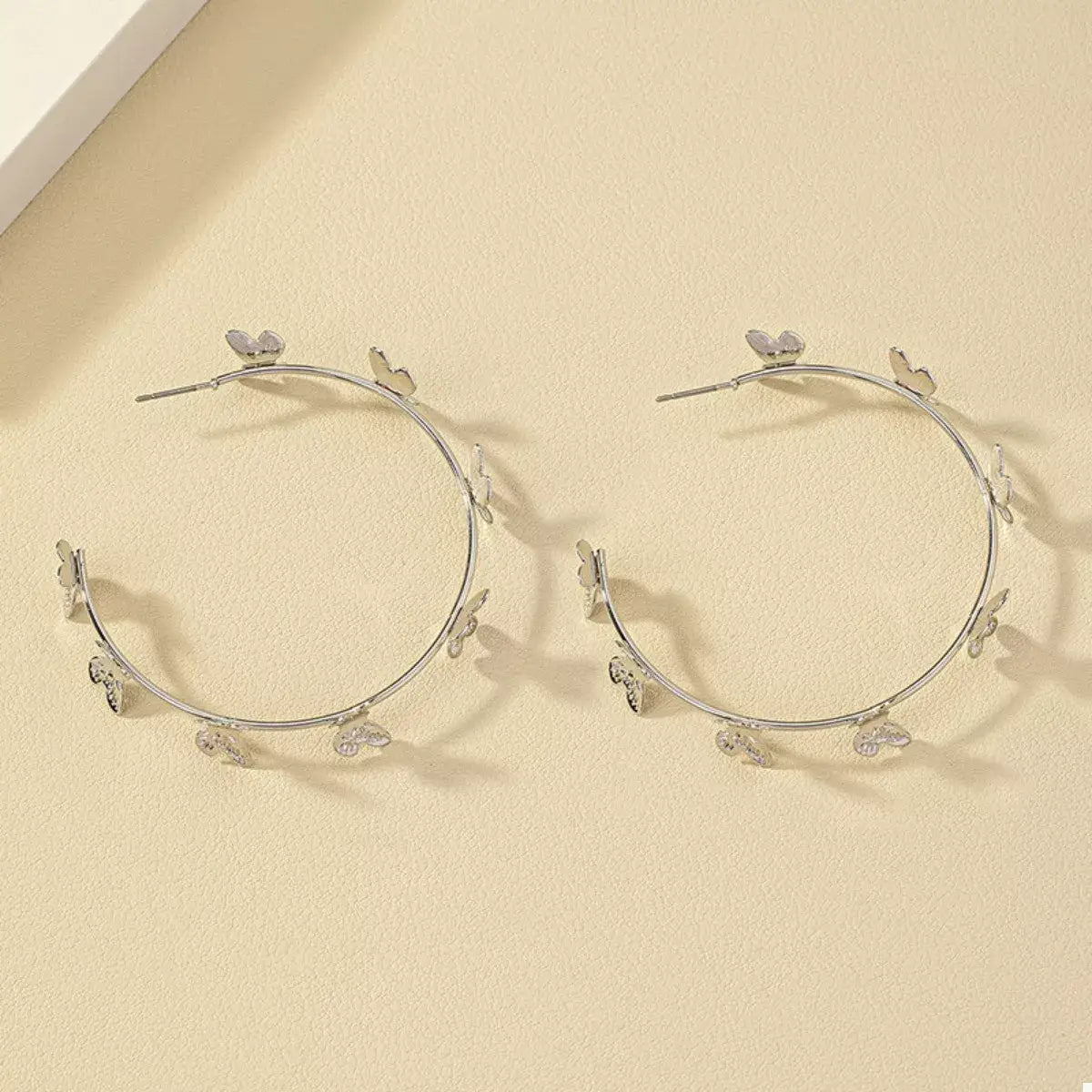 Silver hoop earrings with butterfly charms on a beige background