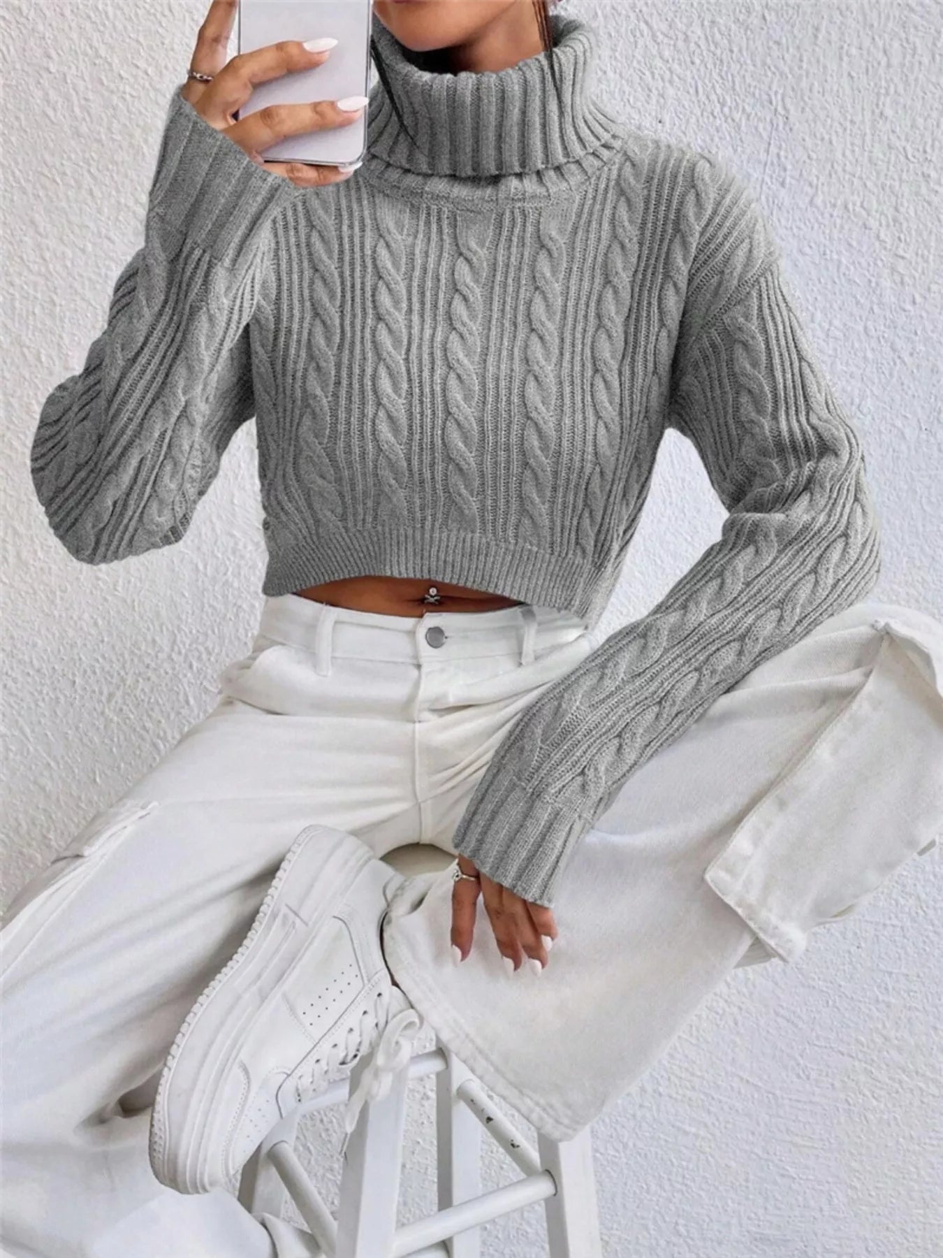 Woman wearing a Cable-Knit Turtleneck Long Sleeve Sweater in gray with a cropped fit, sitting casually.