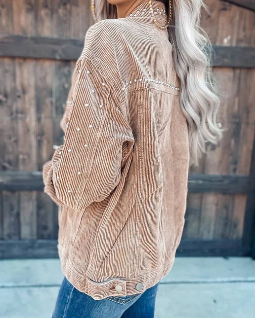 Person wearing a brown corduroy shirt with pearl embellishments against a wooden fence background.