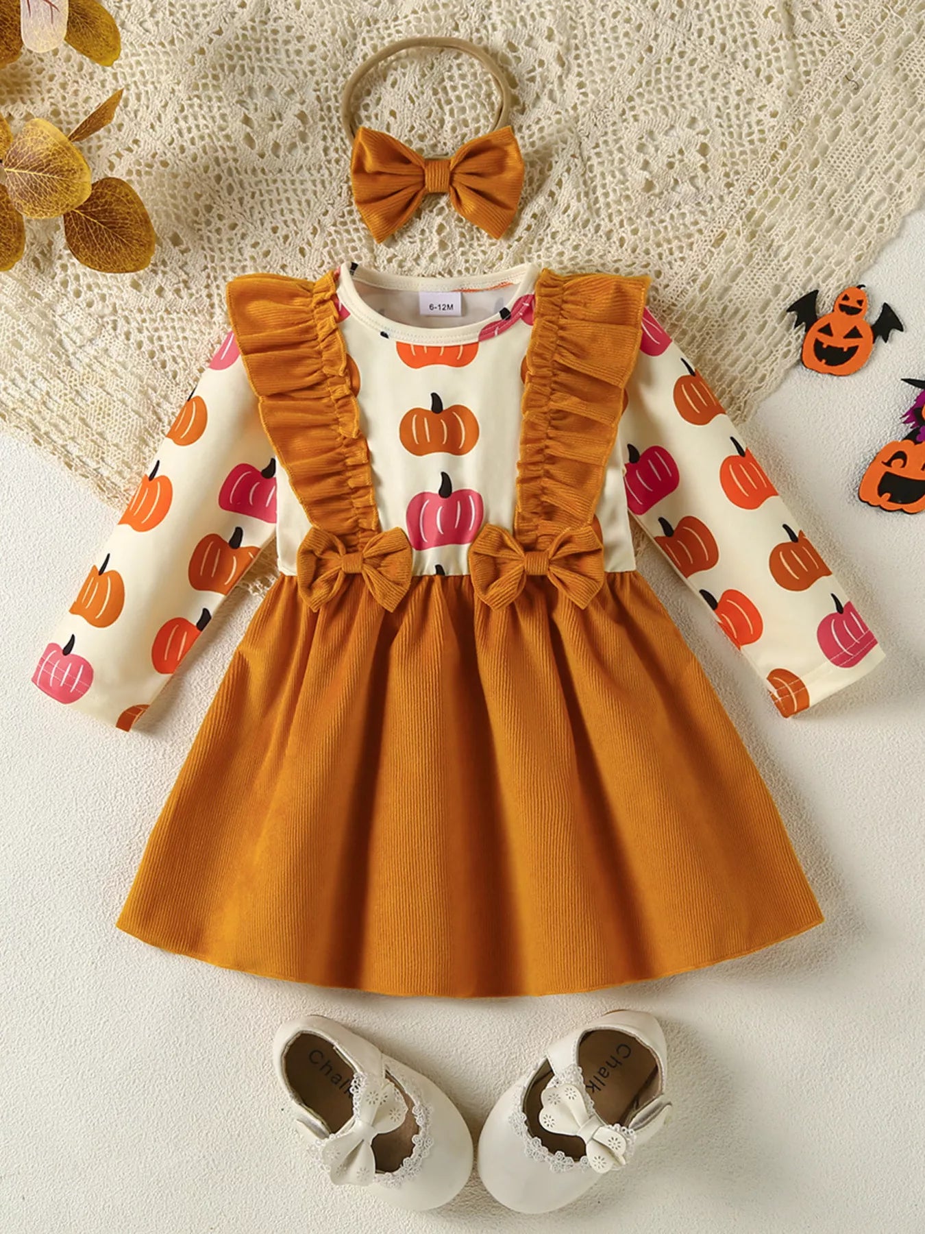 Children's outfit with orange dress, pumpkin-patterned shirt, shoes, and headband on a textured surface.