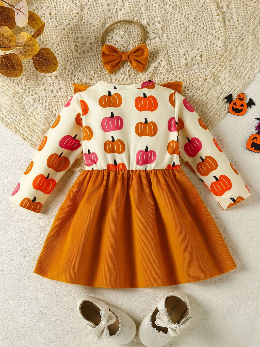 Children's outfit with pumpkin pattern dress, shoes, and headband on a textured surface.
