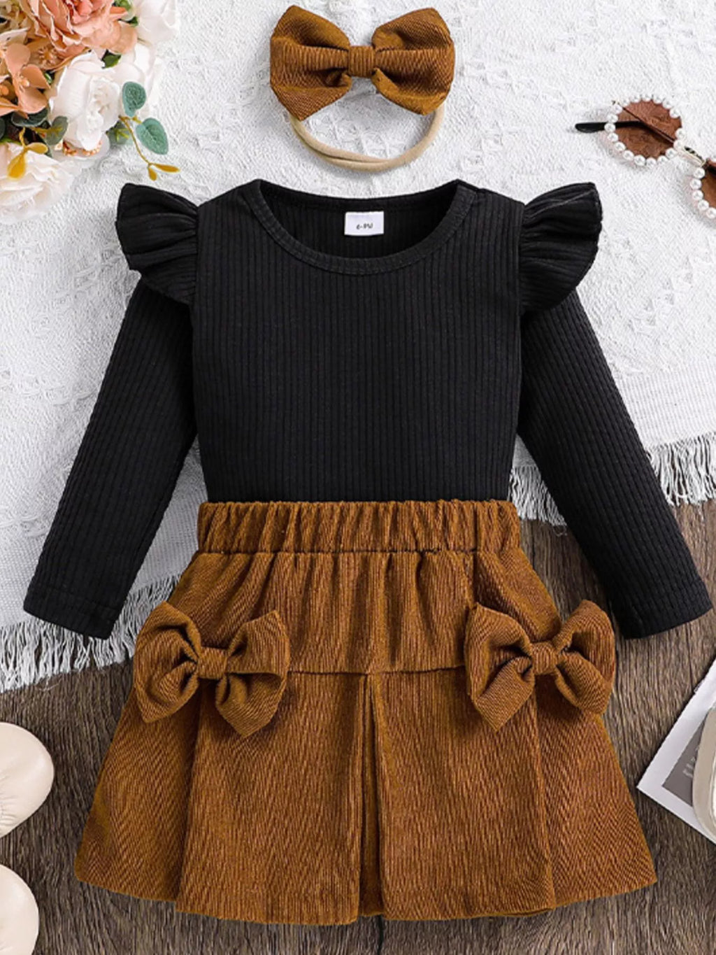 Black long-sleeve top and brown skirt set with a bow headband on a textured surface.