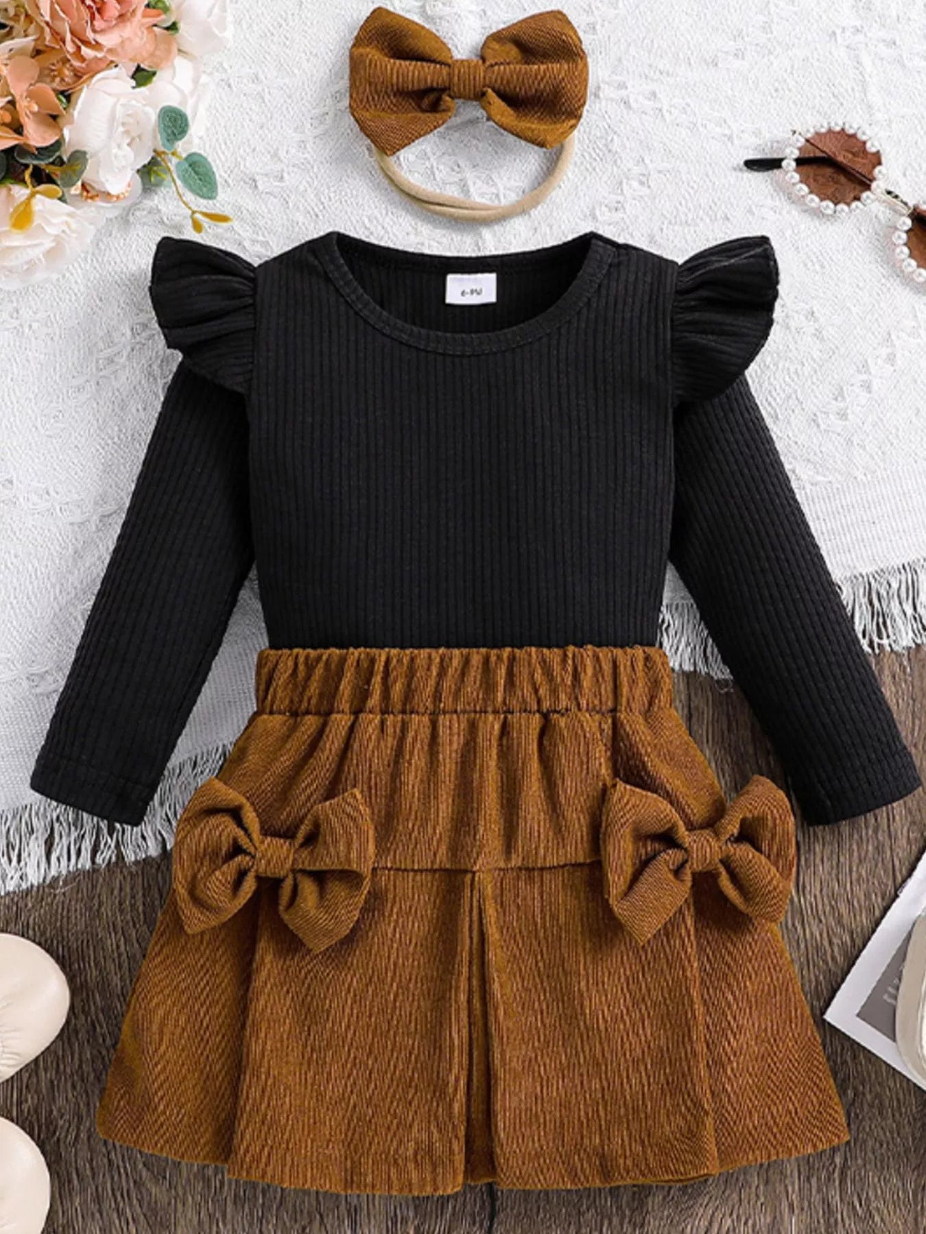 Black long-sleeve top and brown skirt set with a bow headband on a textured surface.