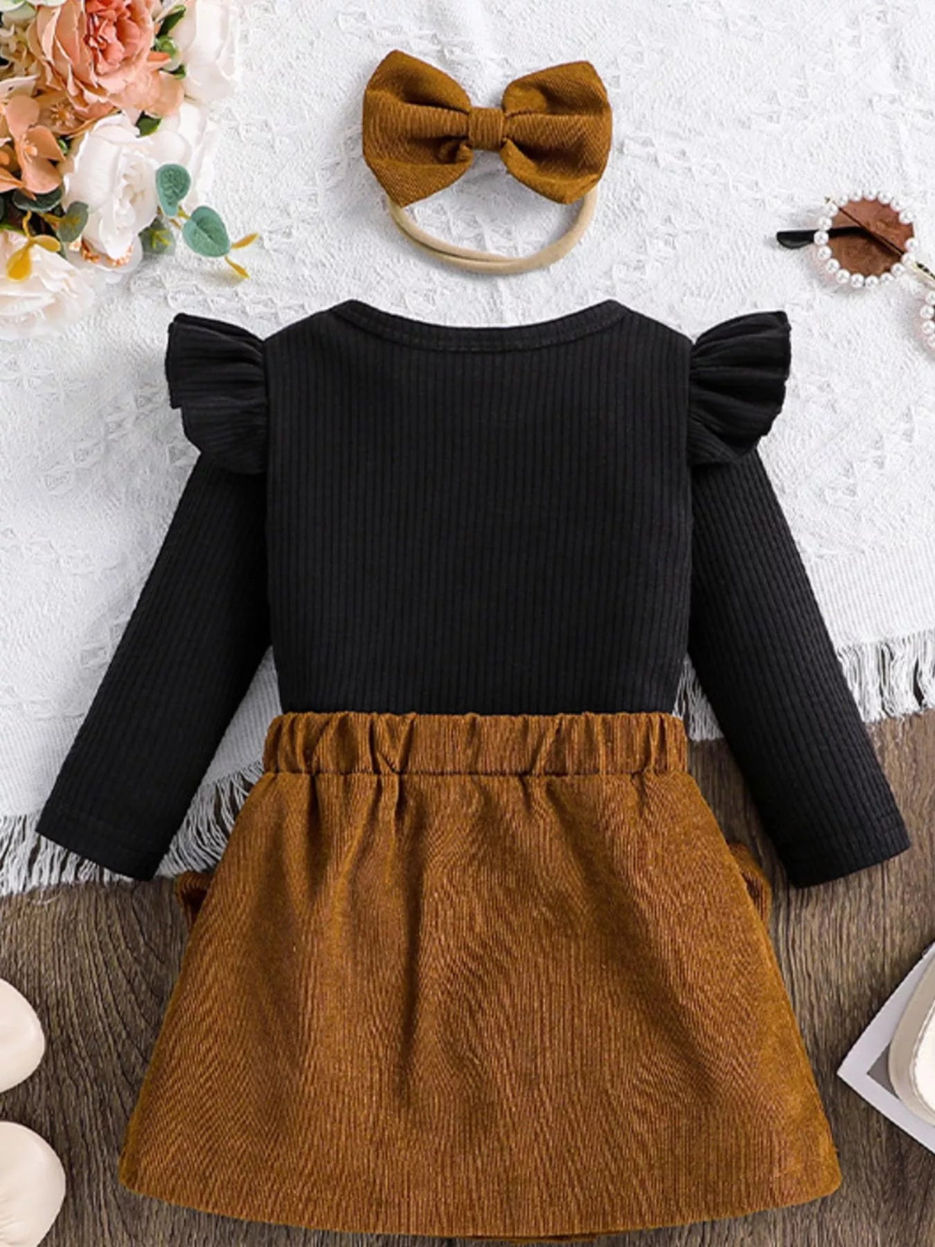 Black top with ruffled sleeves and brown skirt on a white surface with decorative elements.