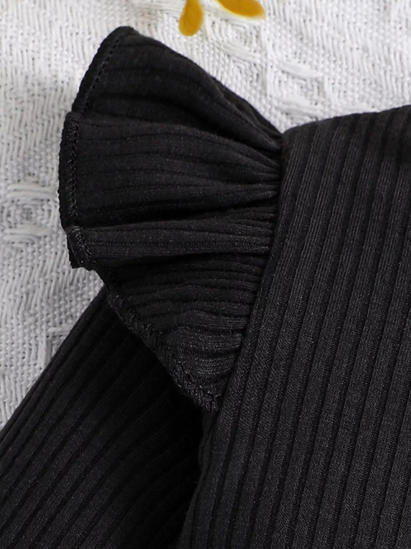 Close-up of a black ribbed sweater with a bow detail on a textured white background