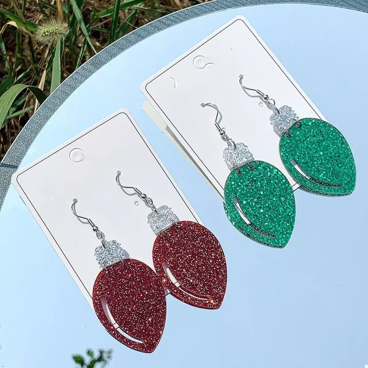 Red and green glittery earrings on display cards with a natural background