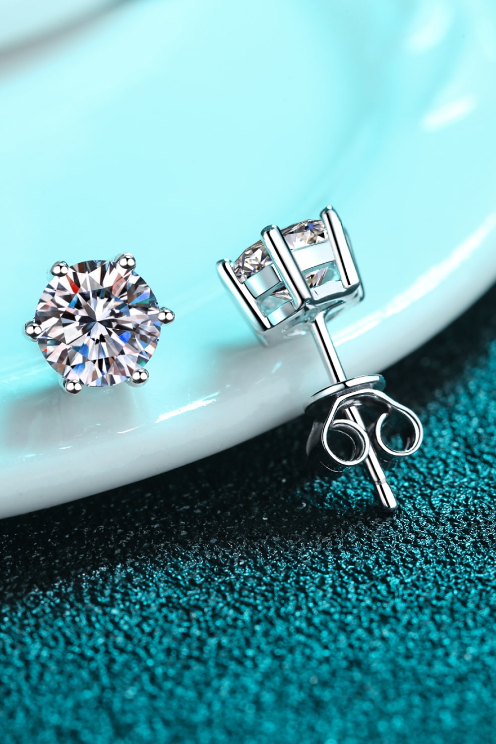 Endless Cheer Moissanite Stud Earrings .2 Carat Two diamond stud earrings on a turquoise surface