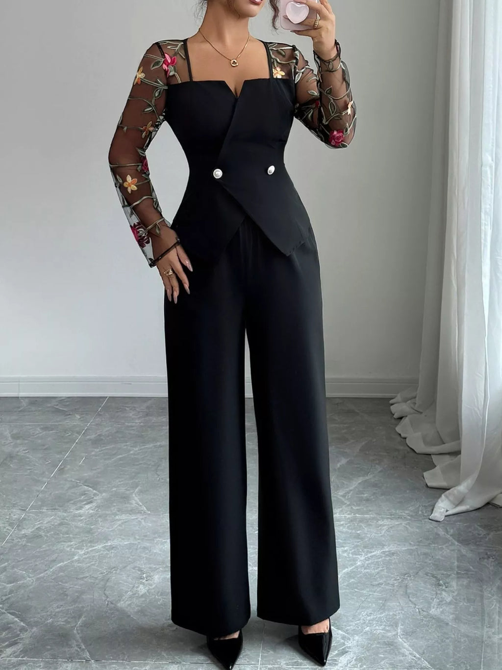 Person wearing a black outfit with floral sleeves against a neutral background