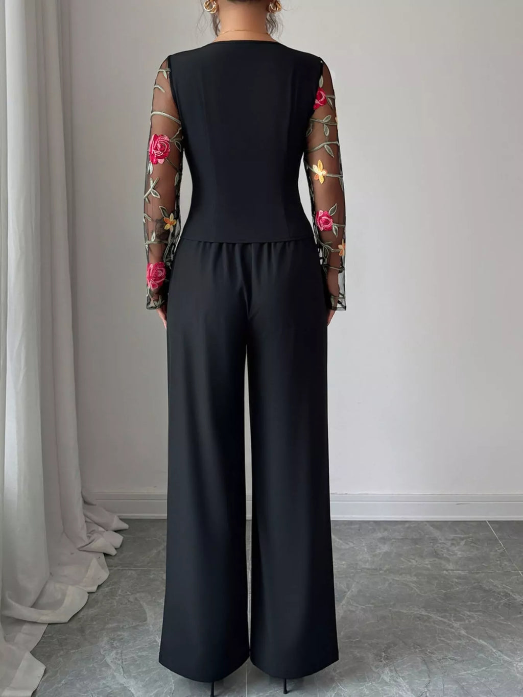 Person wearing a black jumpsuit with floral sleeves against a neutral background