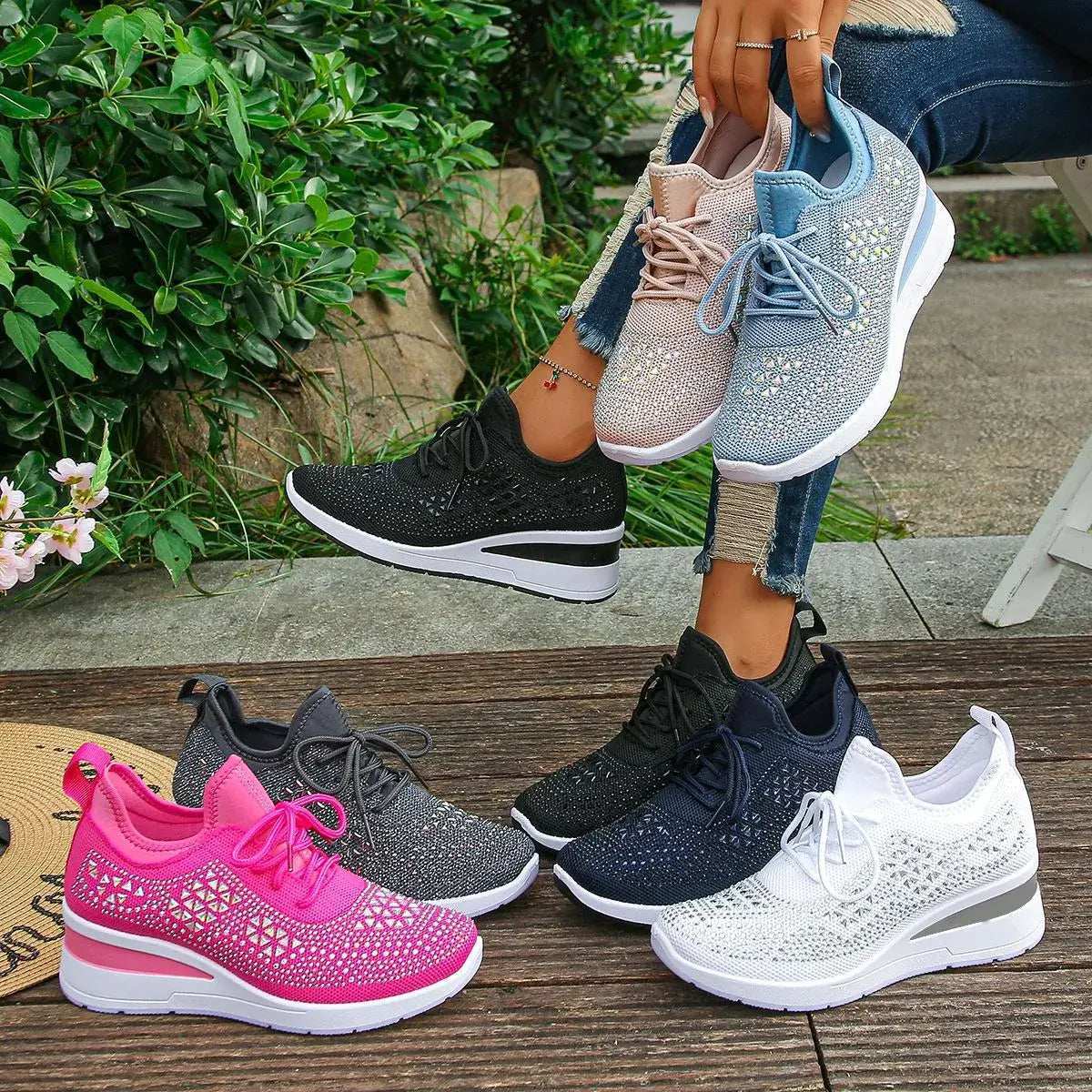 Four pairs of sparkly sneakers in different colors on a wooden surface with a person holding two pairs.