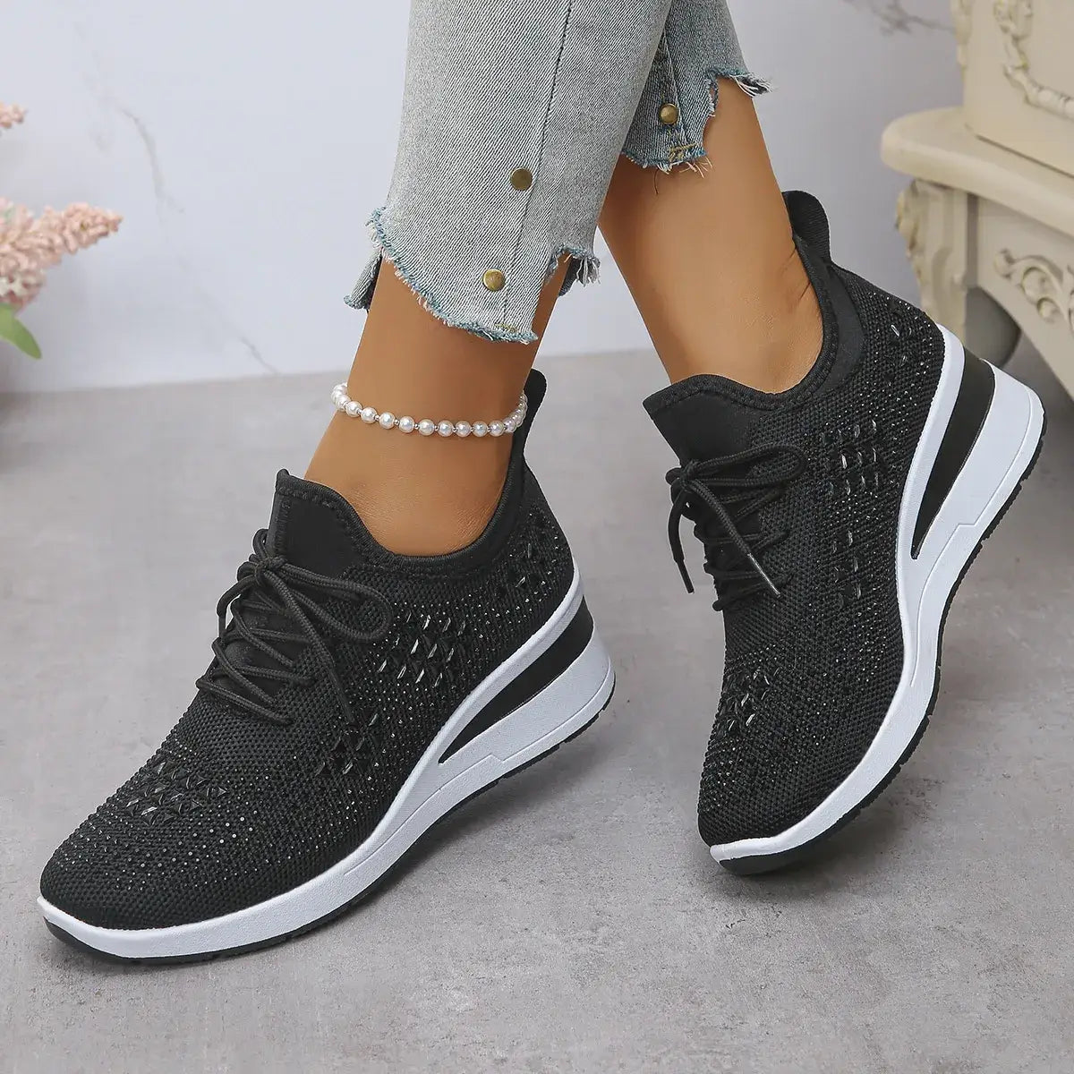 Black sneakers with white soles worn by a person on a light gray floor.