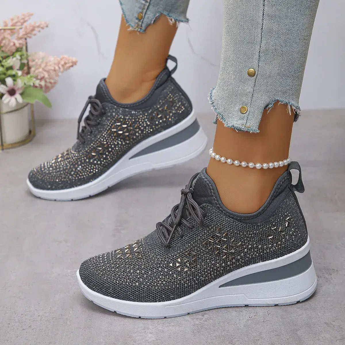 Gray sneakers with rhinestone details worn by a person on a light gray surface.