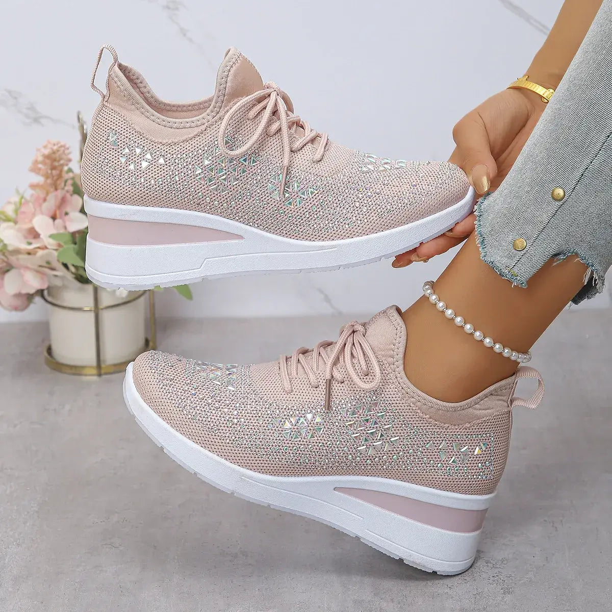 Pink sneakers with rhinestone details worn by a person, with a light background.
