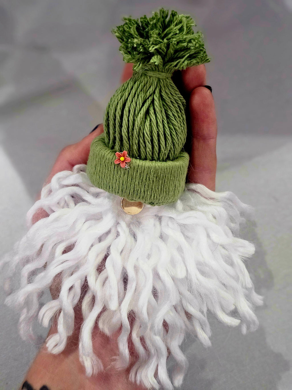 Handmade green knitted hat with white beard held by a person against a neutral background