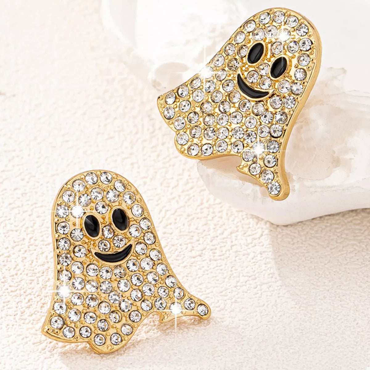 Gold ghost-shaped earrings with rhinestones on a light background