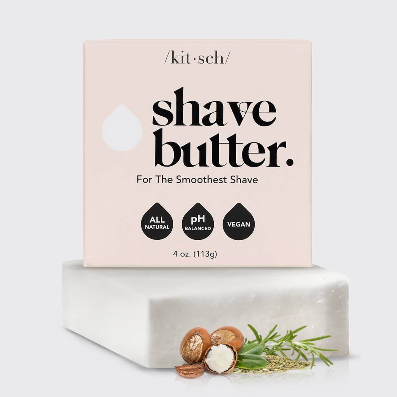 A bar of Kitsch Shave Butter placed on a white surface with nuts and a greenery decoration in the foreground, and a pink packaged label that reads 'shave butter. For The Smoothest Shave', indicating all natural, pH balanced, and vegan properties.