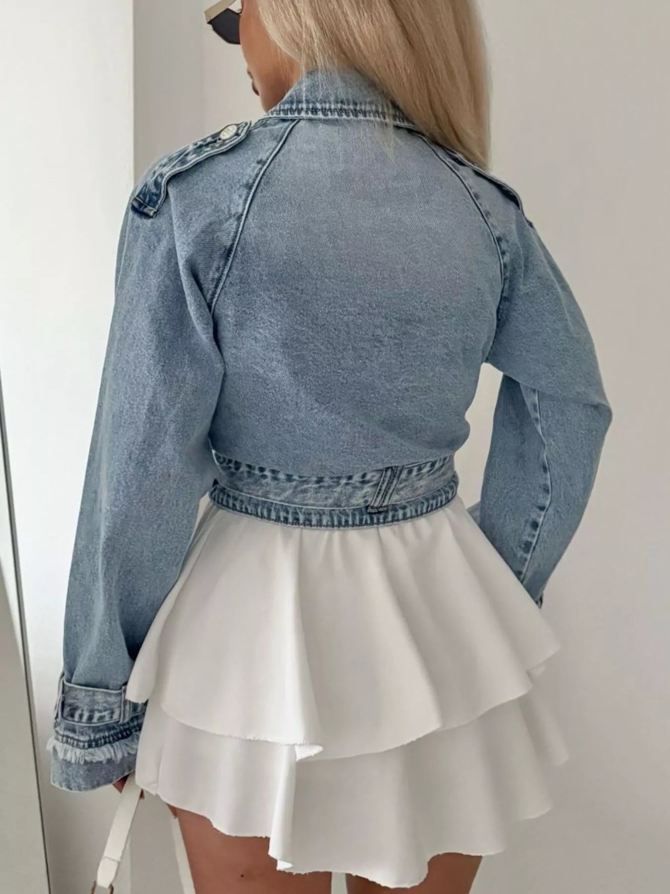 Person wearing a denim jacket over a white dress against a neutral background