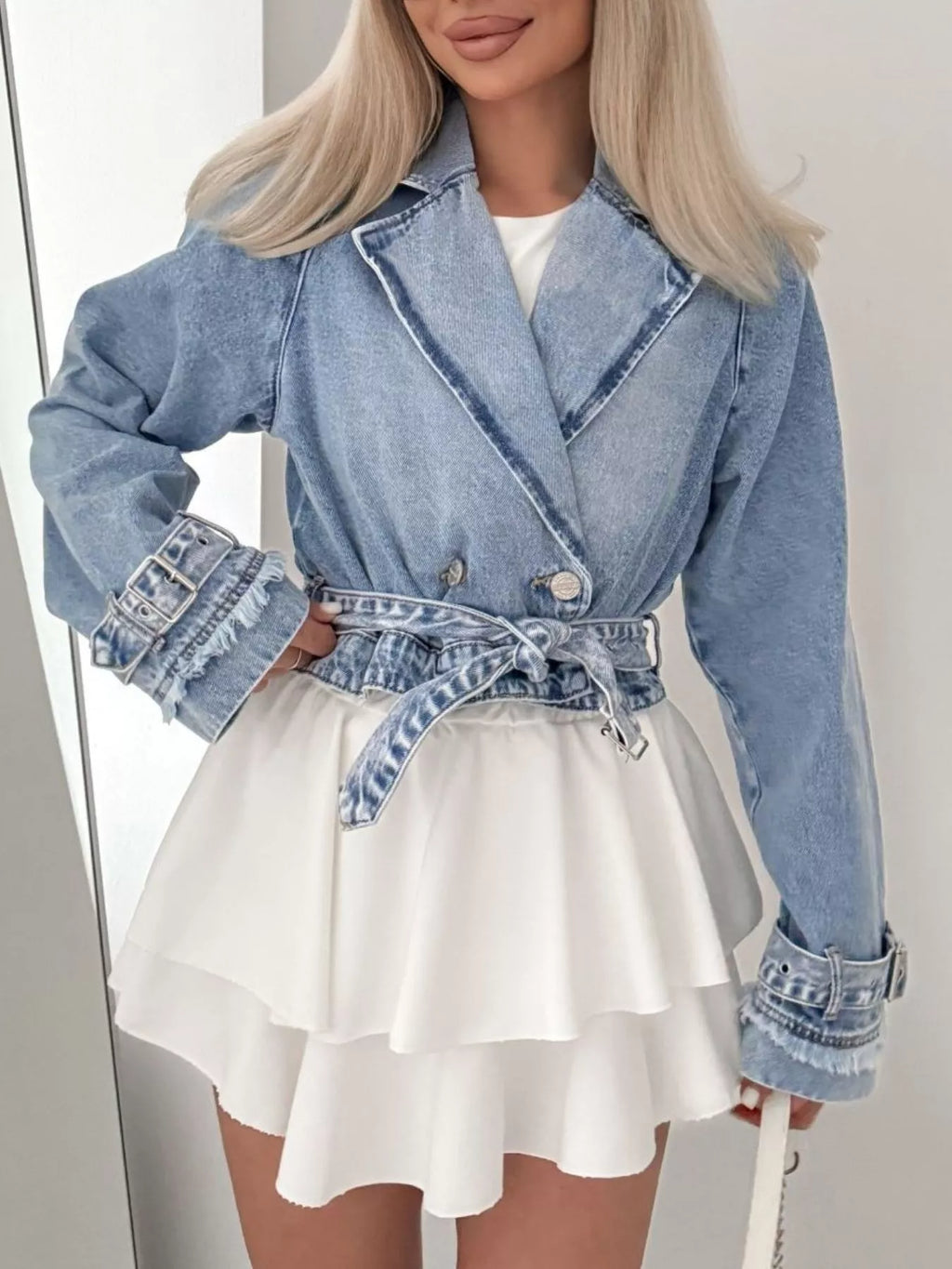 Person wearing a blue denim jacket and white dress against a neutral background