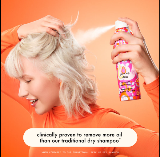 Person applying dry shampoo to their hair with an orange background