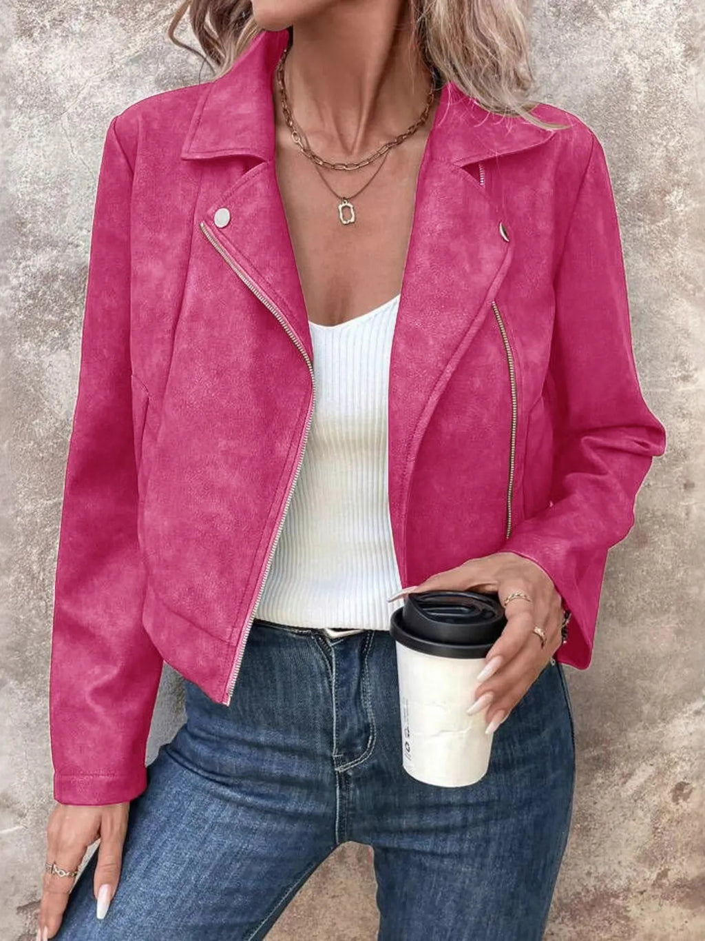 Person wearing a pink suede jacket holding a coffee cup against a neutral background