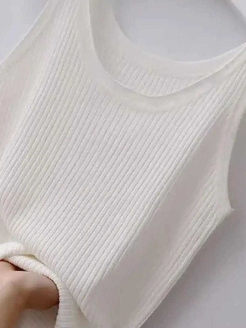 Close-up of a white ribbed knit garment held by a hand against a white background