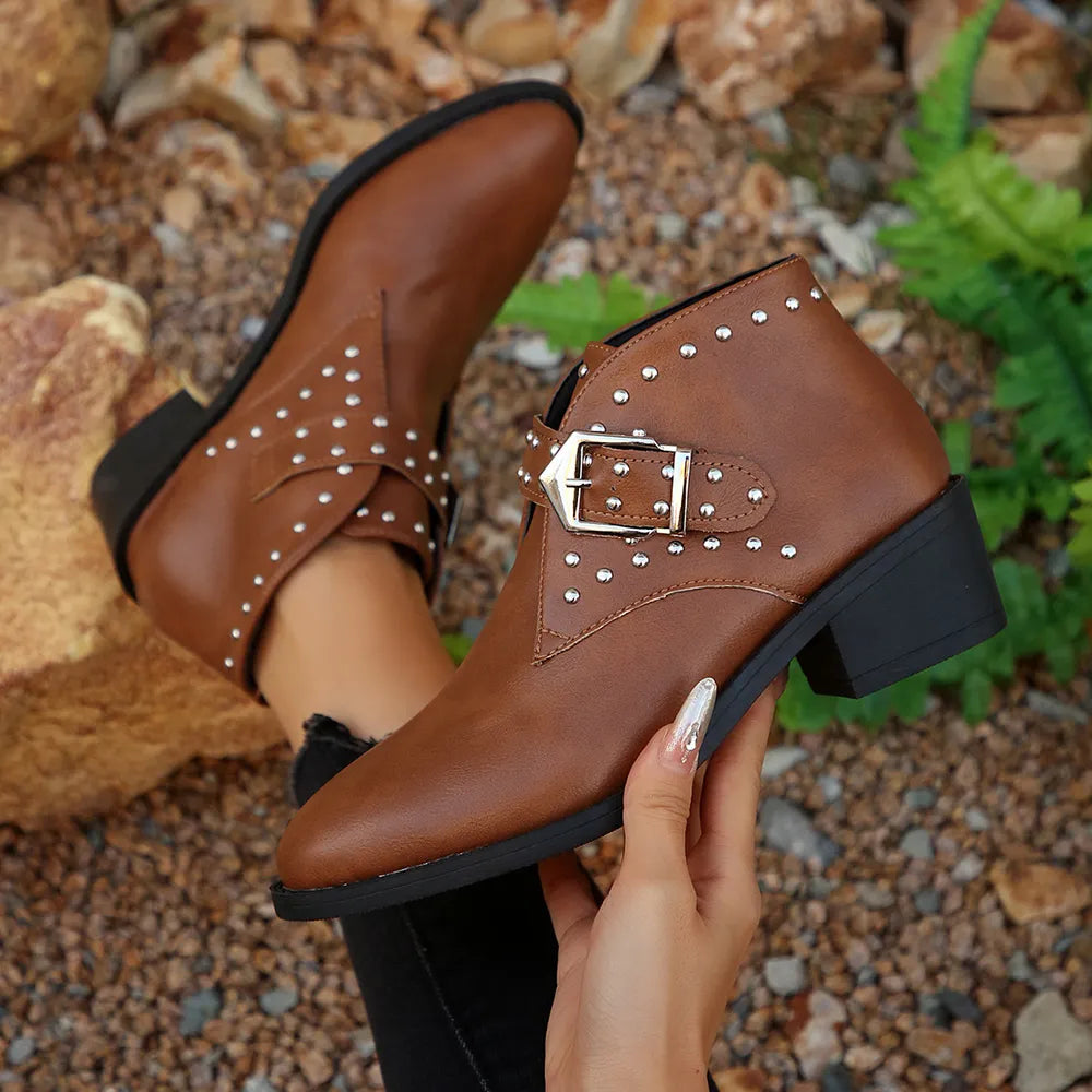 Brown leather boots with studded details and a buckle held by a hand against a natural background.