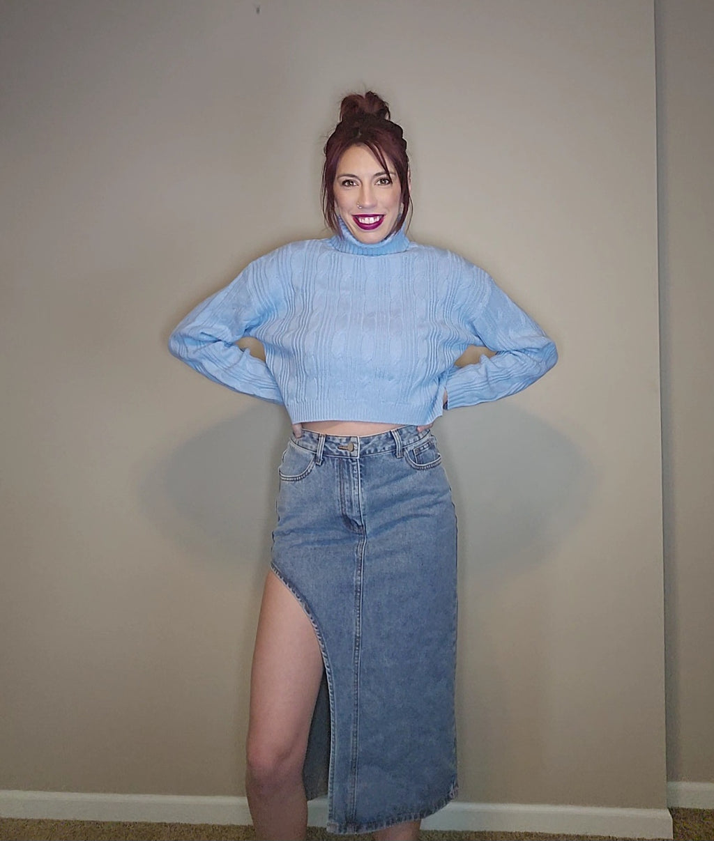 Model wearing a light blue sweater with a thigh slit denim skirt, showcasing trendy fashion.