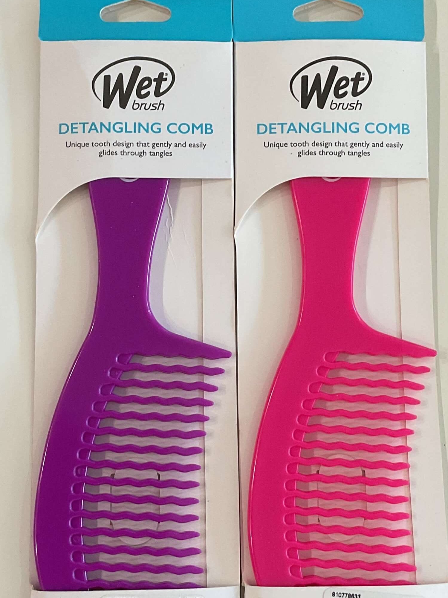 Two Wet detangling combs in packaging on a white surface with a tiled floor background.