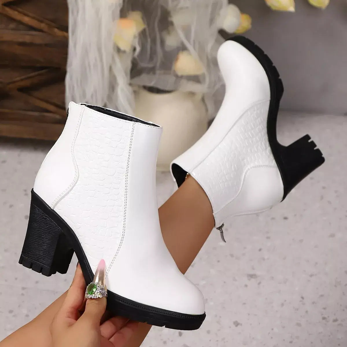 White ankle boots with black soles held by a hand on a neutral background