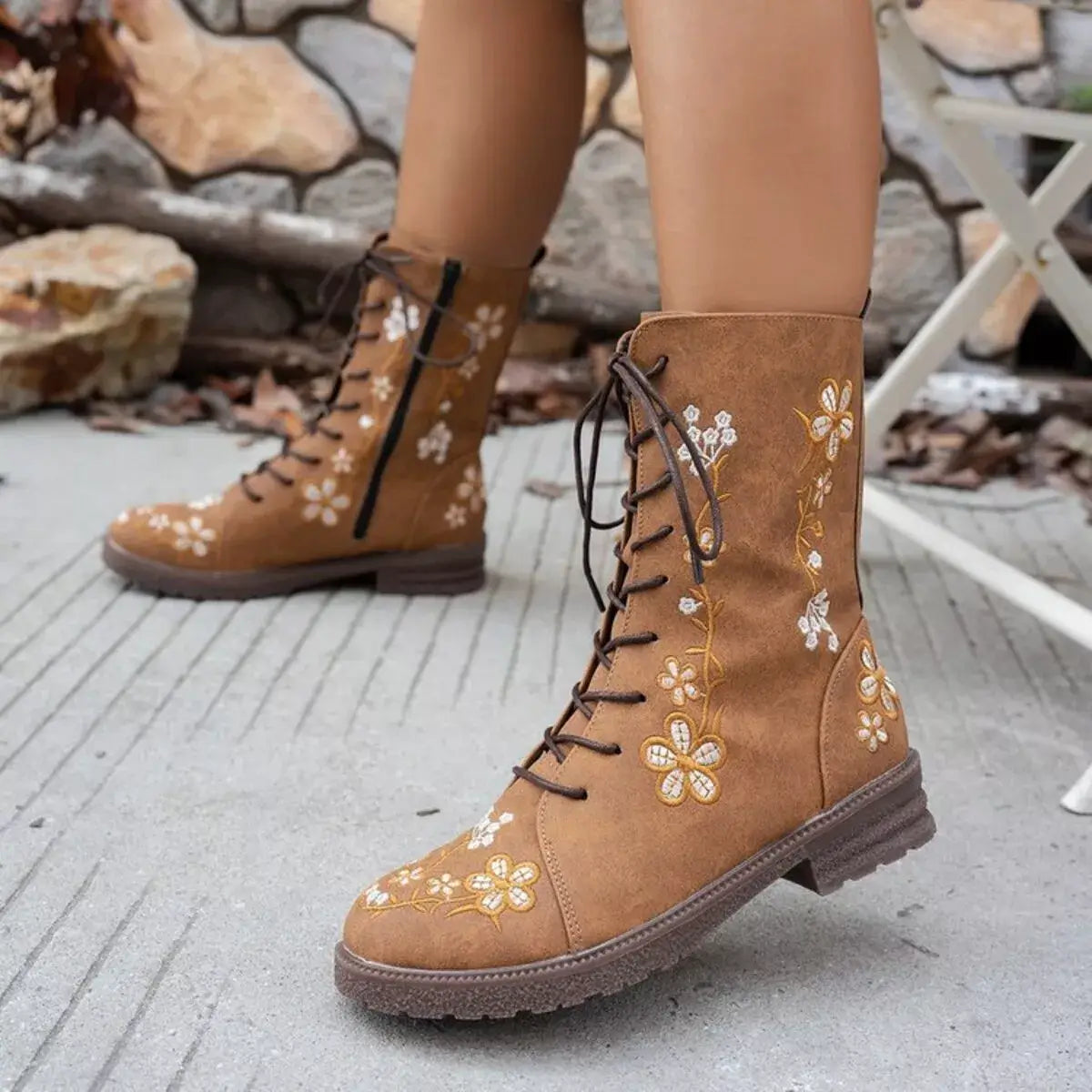 Brown lace-up boots with floral embroidery on a stone surface.