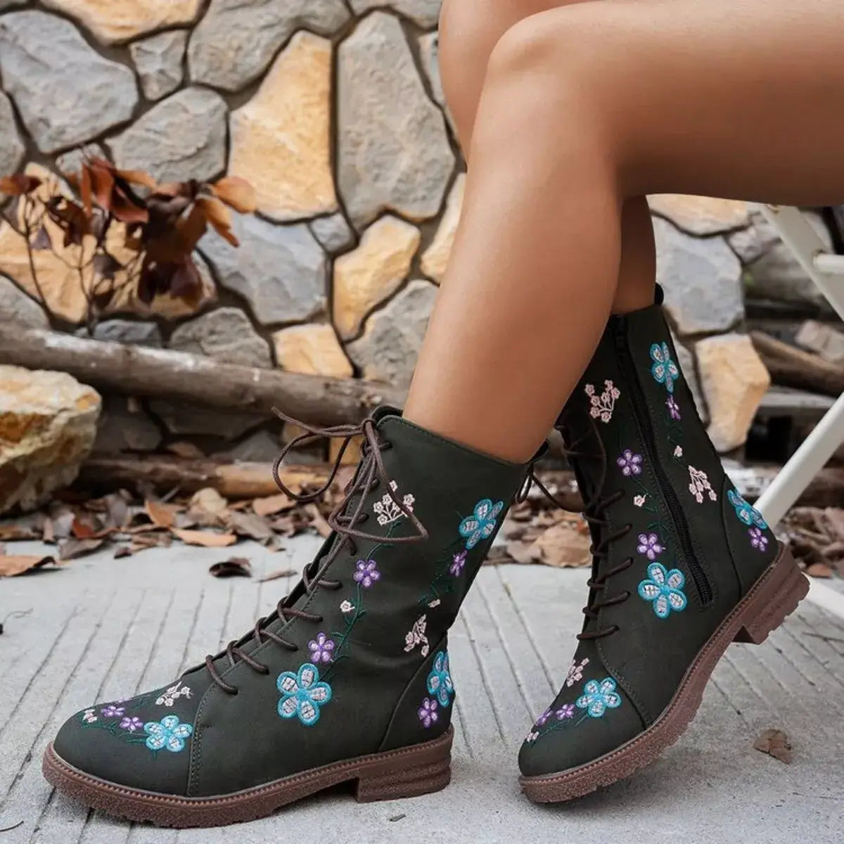Black floral embroidered boots worn by a person sitting against a stone wall.