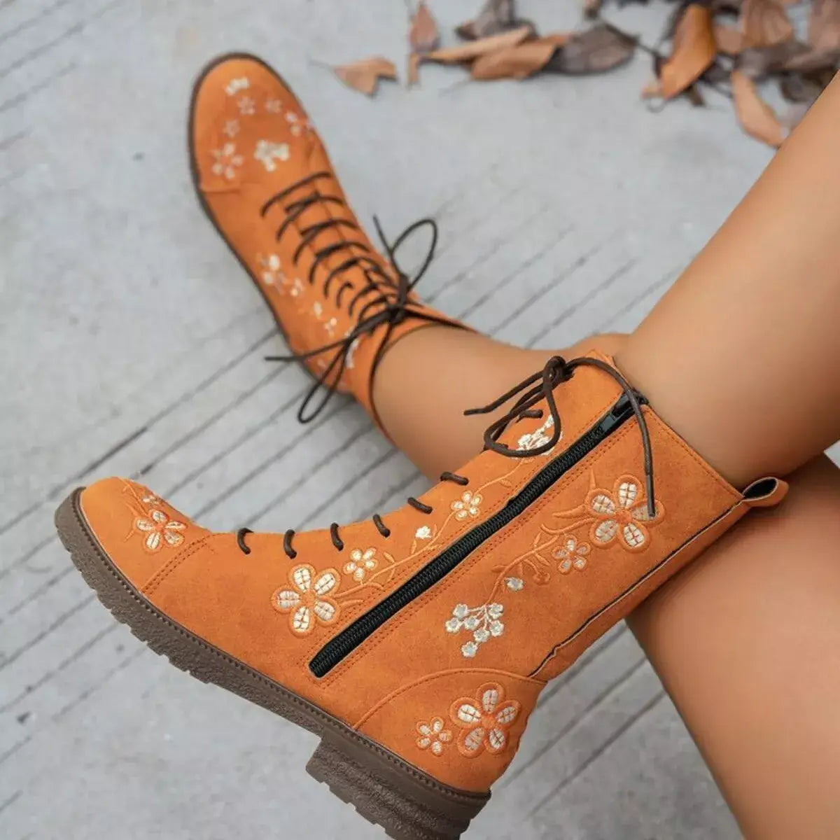 Orange boots with floral embroidery on a light gray surface
