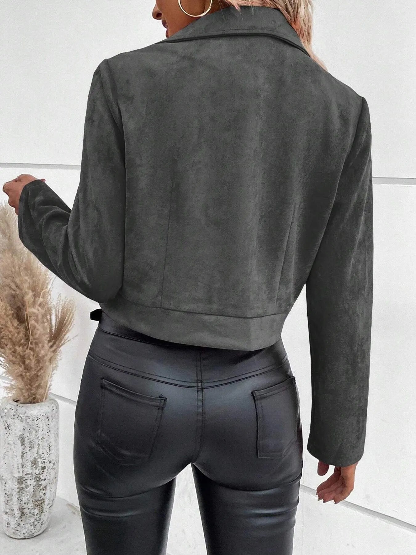 Person wearing a gray suede jacket and black leather pants against a white background