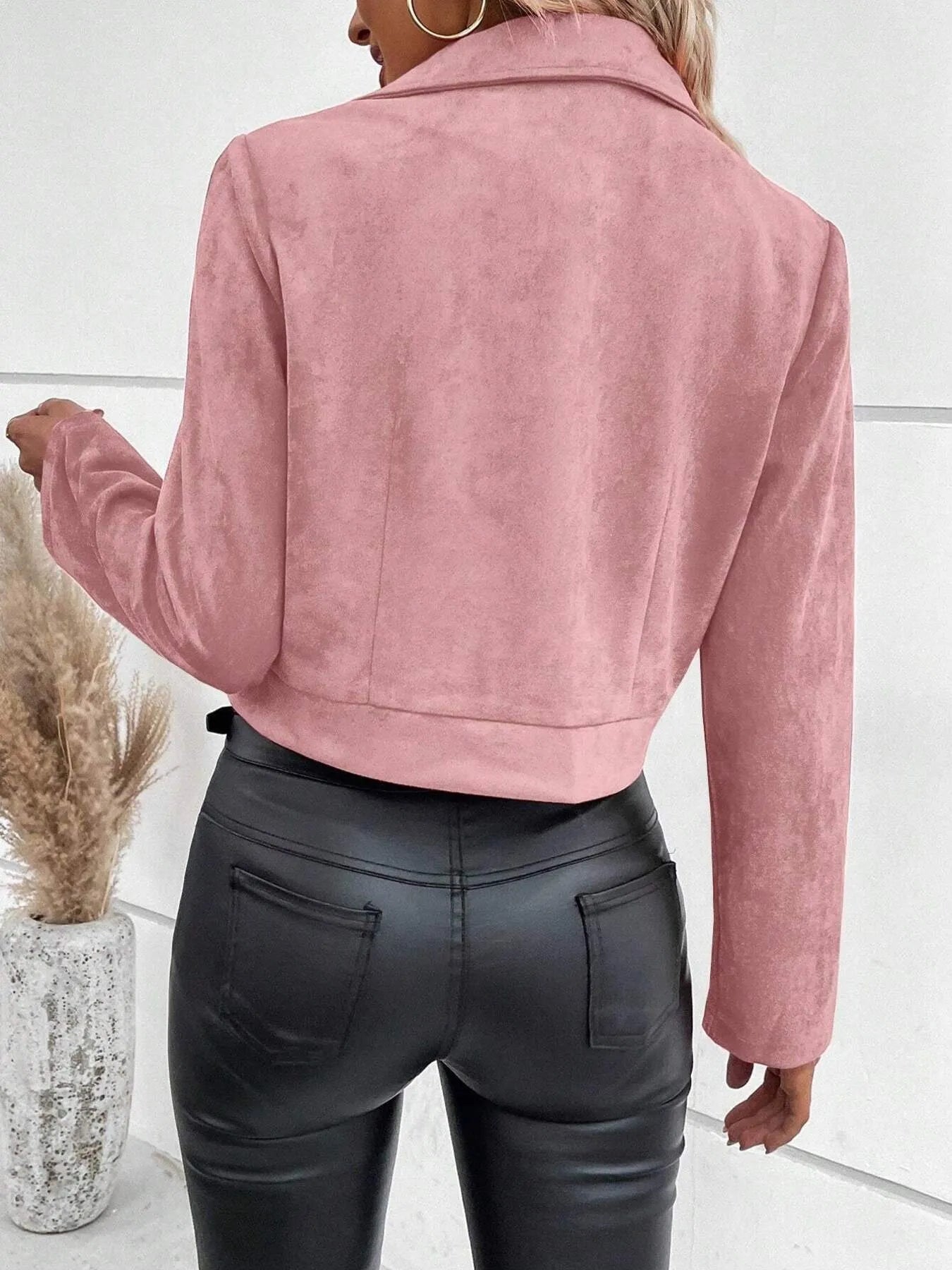 Person wearing a pink suede jacket and black leather pants against a white background
