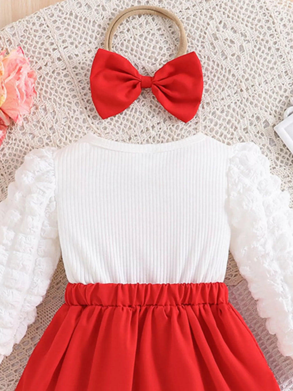 White long-sleeve top with red skirt and red bow headband on a textured surface.