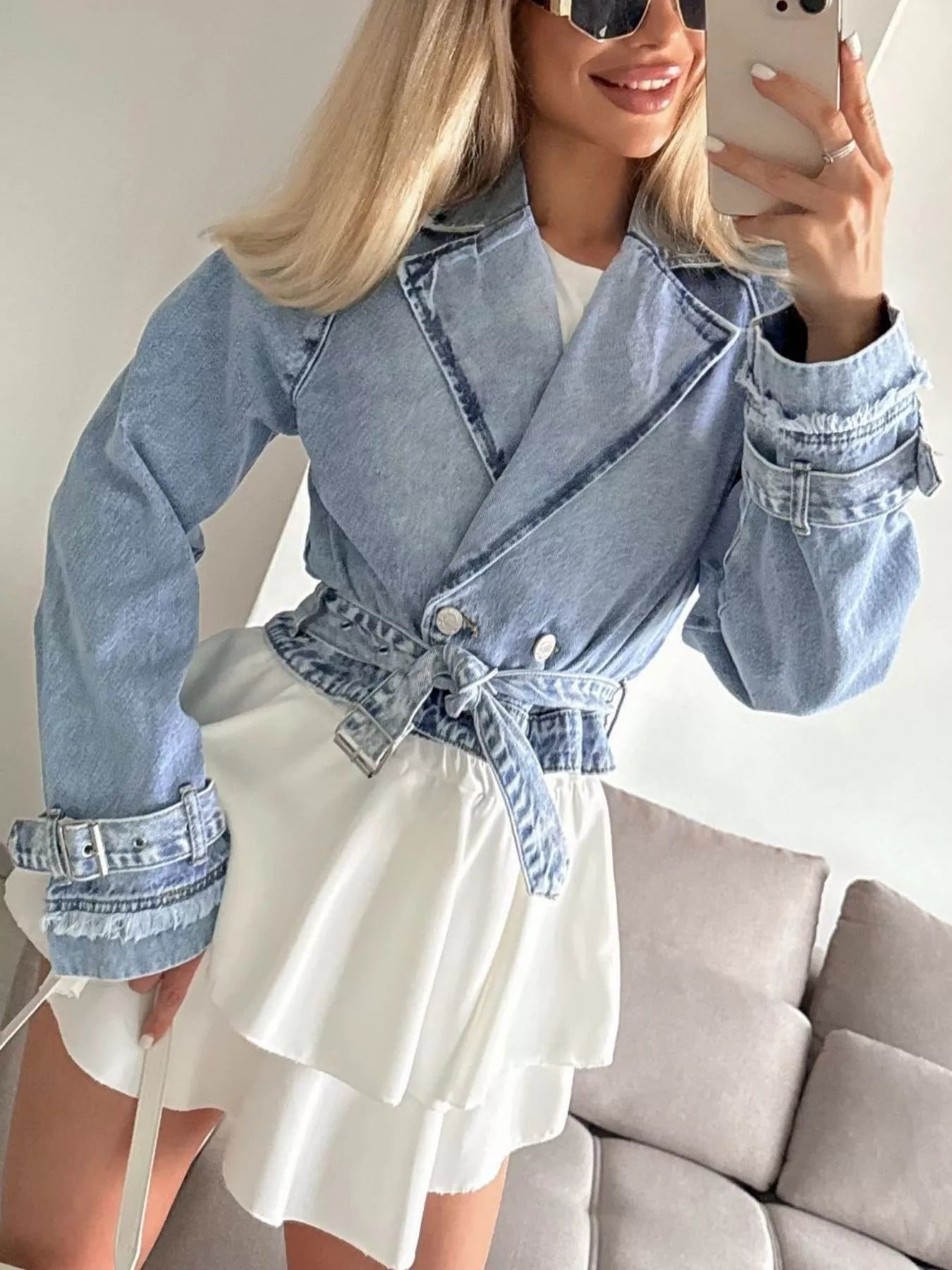 Woman wearing a denim jacket and white dress, taking a selfie.