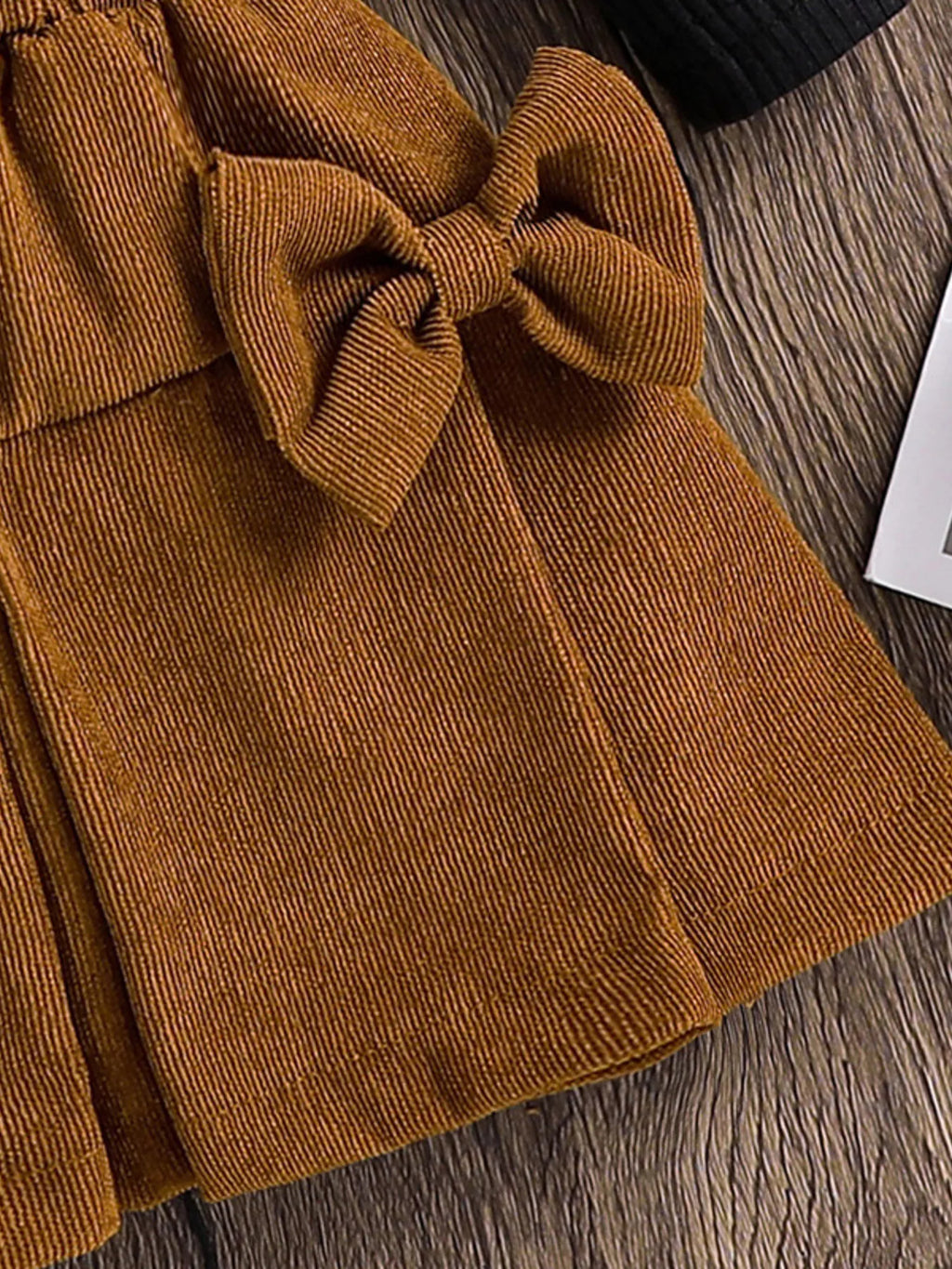Brown corduroy skirt with a large bow on a wooden surface