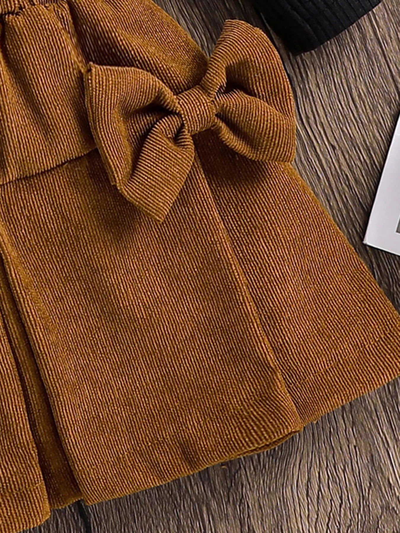 Brown corduroy skirt with a large bow on a wooden surface