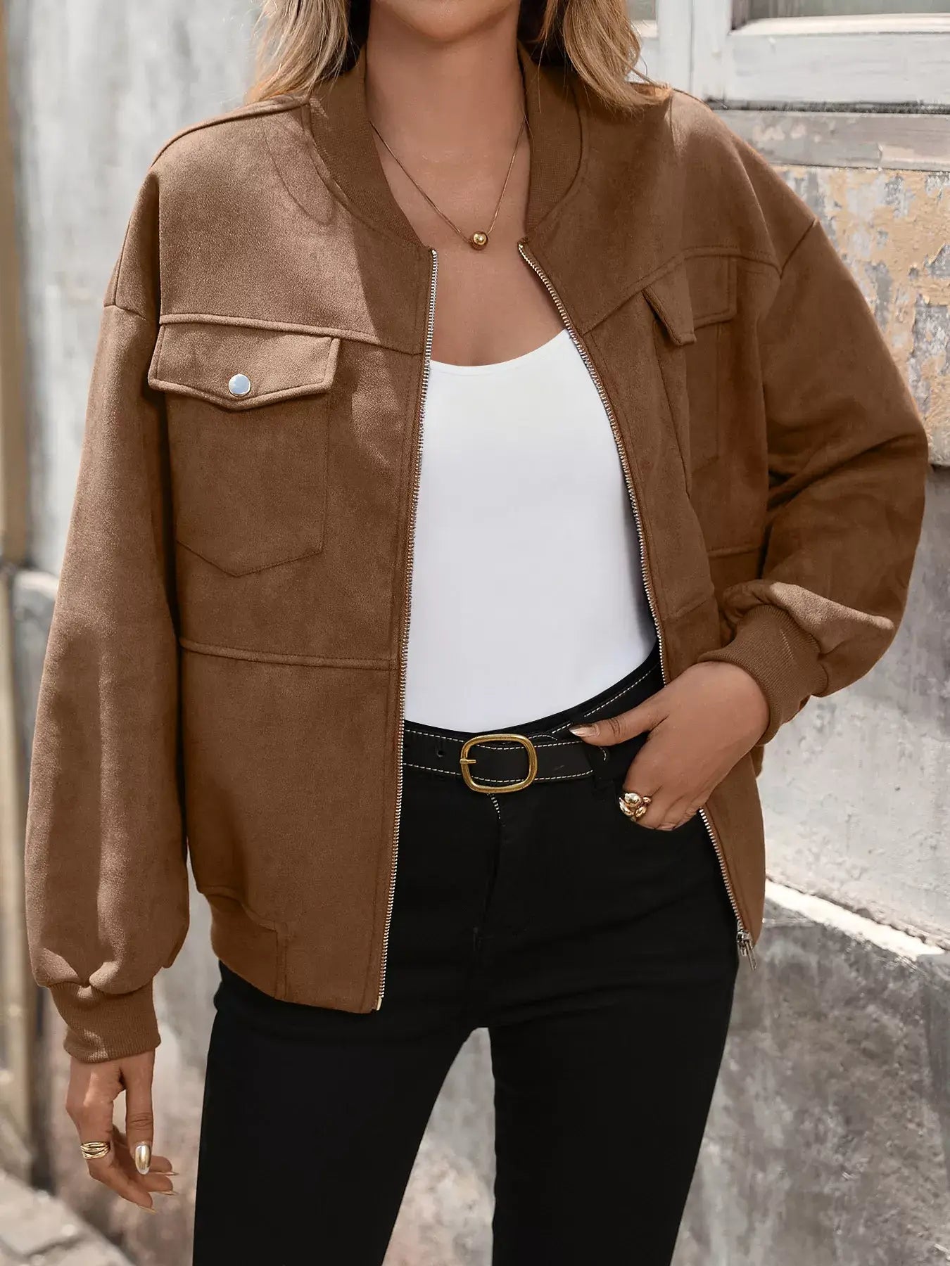 Person wearing a brown jacket over a white top and black pants.
