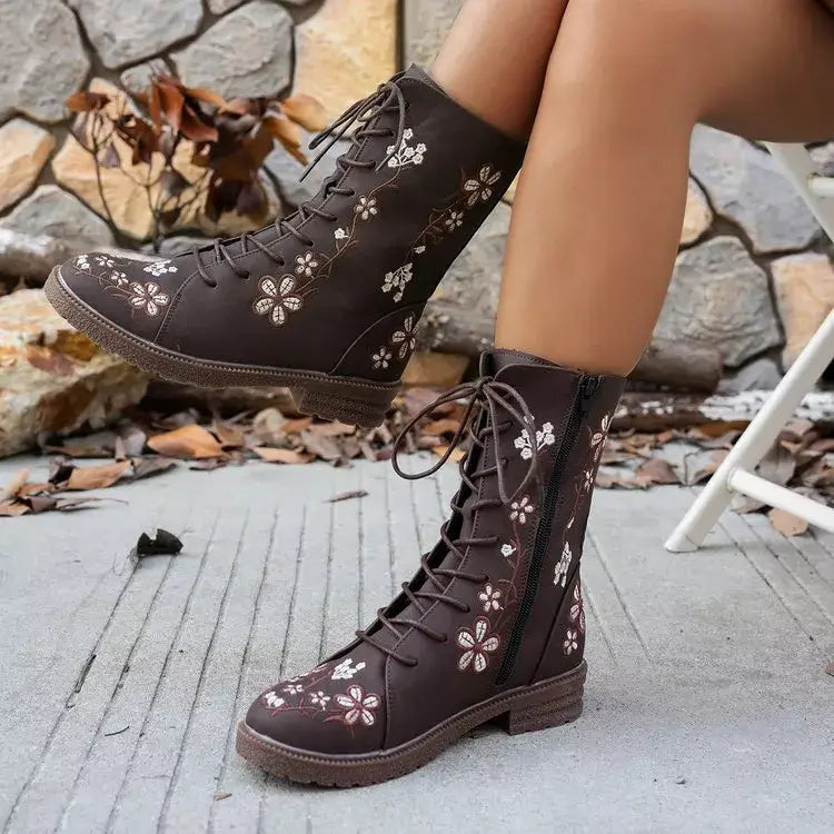 Brown lace-up boots with floral patterns worn by a person outdoors.