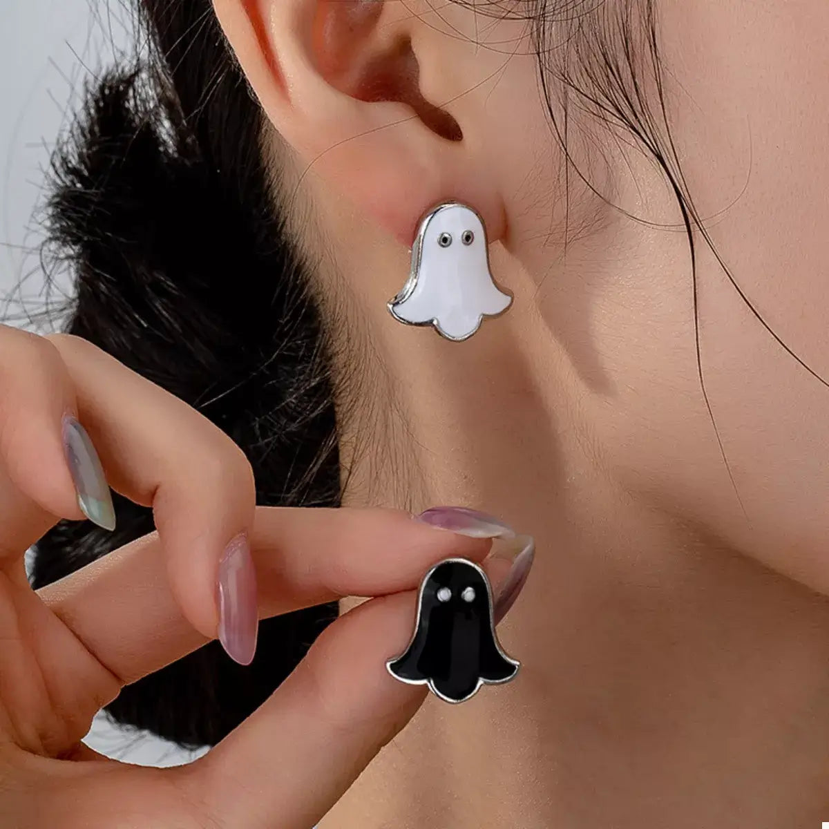 Ghost-shaped earrings being worn and held up to the ear.